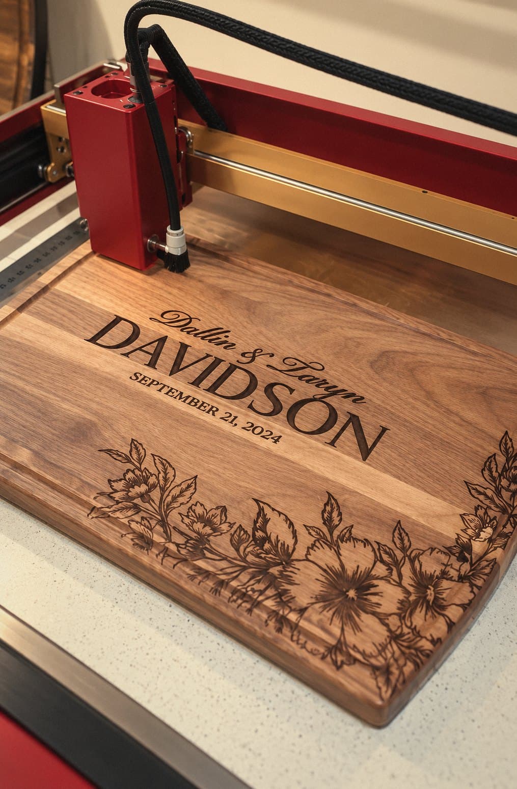 Walnut wedding cutting board being laser engraved with names, a date and florals